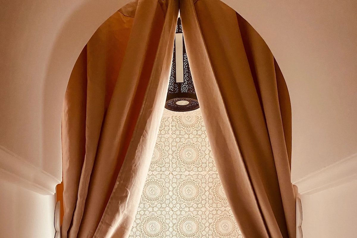 A bedroom with a bed, a bedside table with a vase of flowers, and a patterned wall.