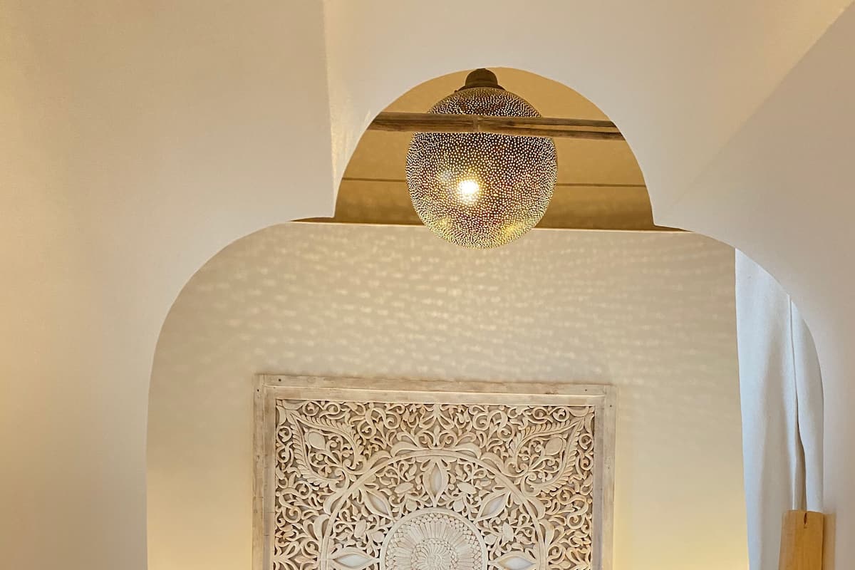 A bed with a decorative headboard, two bedside lamps, and a hanging light fixture.