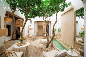 Un patio tranquilo con piscina, mobiliario de mimbre e iluminación colgante.