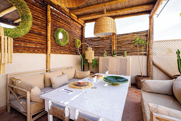Un espacio exterior para comer con una mesa blanca dispuesta para dos, rodeado de asientos acolchados.