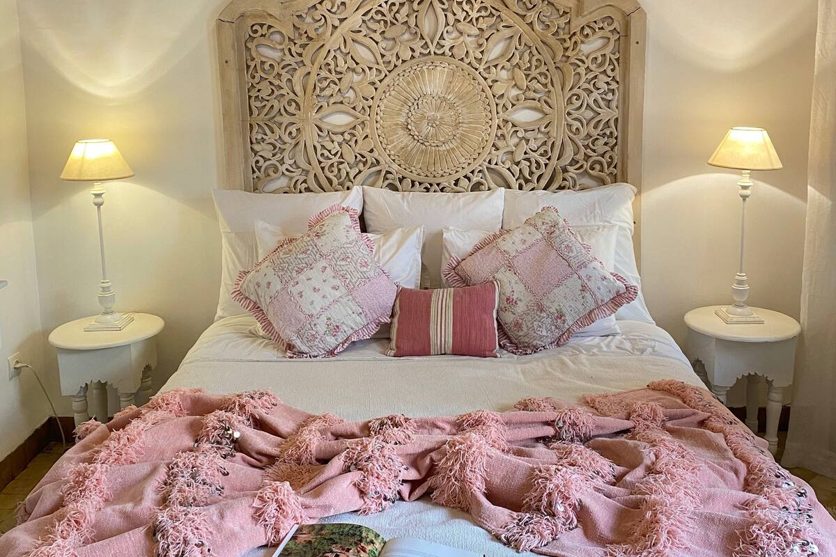 A bed with an ornate headboard, two bedside tables with lamps, and a pink blanket.