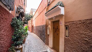 Un estrecho callejón empedrado flanqueado por edificios, con una puerta que tiene un letrero, un ventanal pequeño y un toldo decorativo.