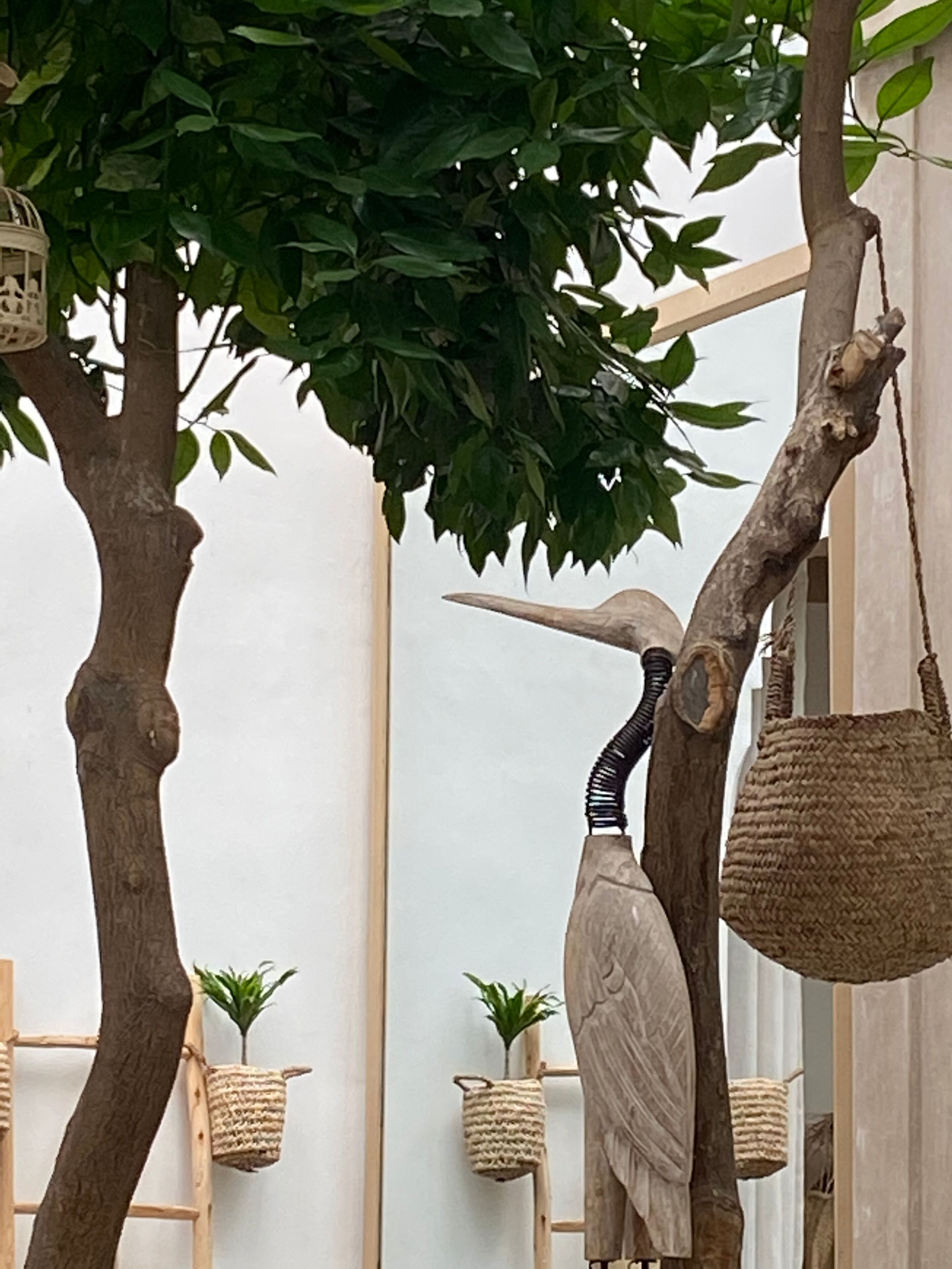 Una habitación con una escalera de madera, una cesta colgante y una escultura de pájaro.