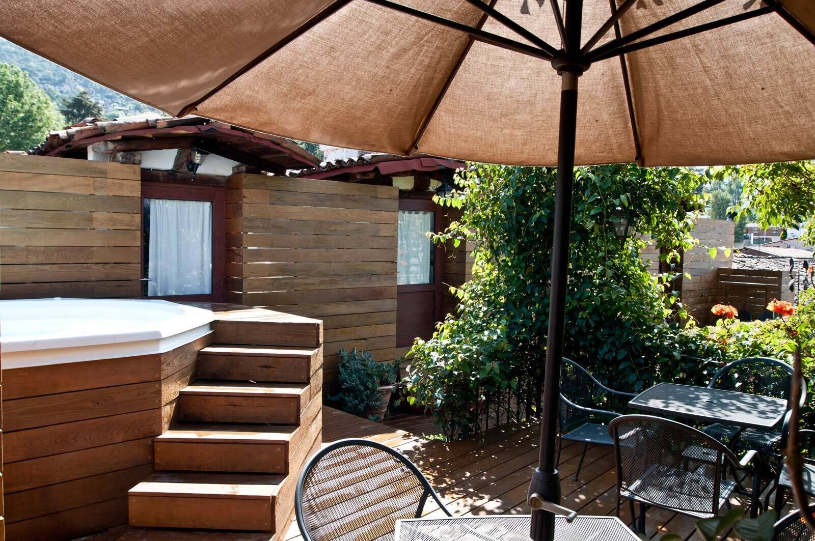 Une terrasse en bois avec un jacuzzi, des sièges d’extérieur et une pergola offrant de l’ombre.