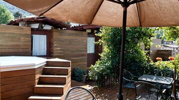 Une terrasse en bois avec un jacuzzi, des sièges d’extérieur et une pergola offrant de l’ombre.