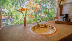 Une salle de bain avec un grand lavabo, un vase avec une fleur et une machine à café.