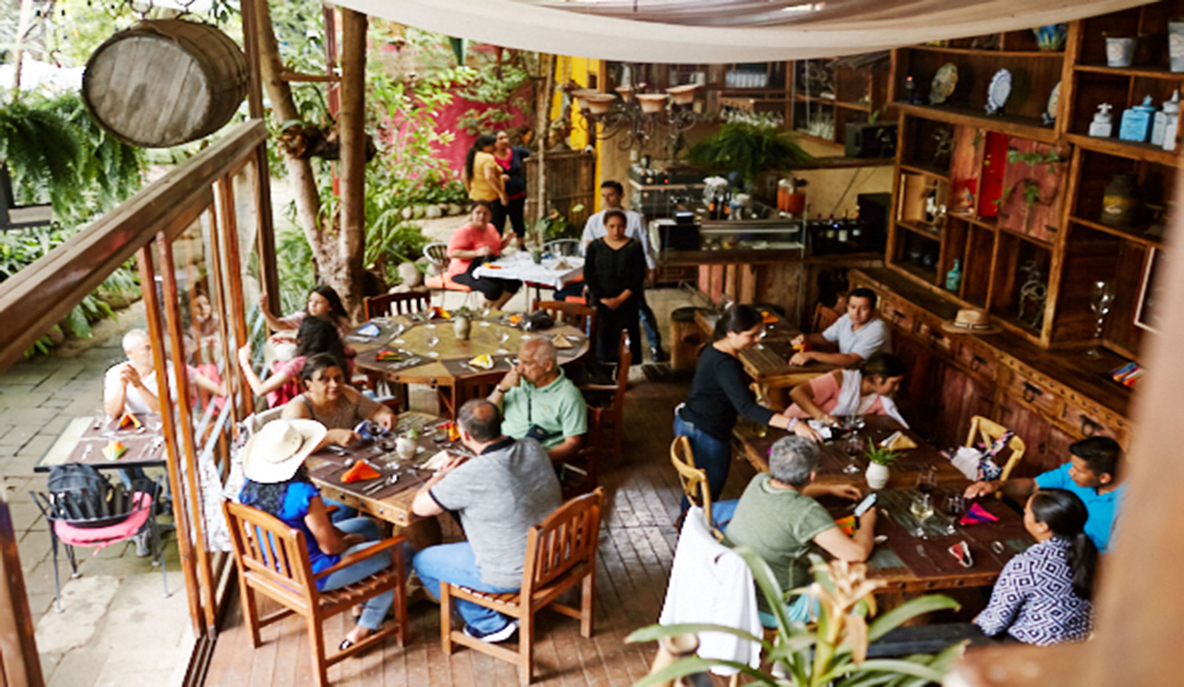 Un área de comedor al aire libre con mesas y sillas de madera, rodeada de vegetación y una estructura rústica de madera.