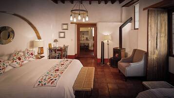A cozy hotel room with a large bed, a bench, a chair, a table, and a fireplace.