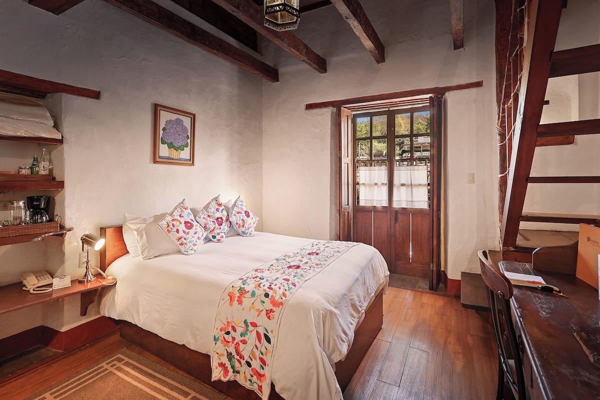 A bedroom with a bed, bedside table, lamp, and a window with a view.