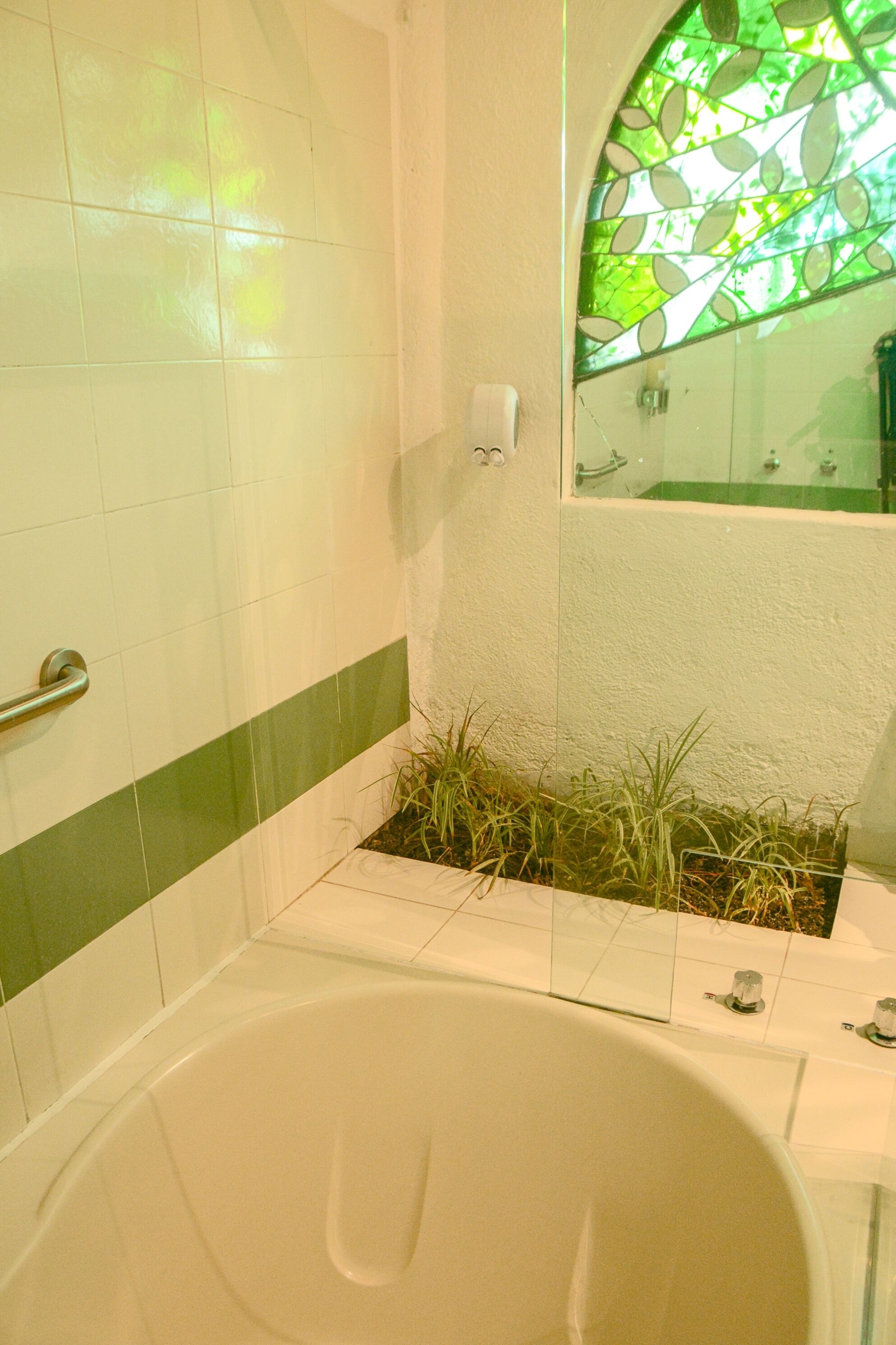 Un baño con bañera, una franja verde en la pared y un ventanal con diseño de hojas verdes.