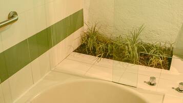 Un baño con bañera, una franja verde en la pared y un ventanal con diseño de hojas verdes.