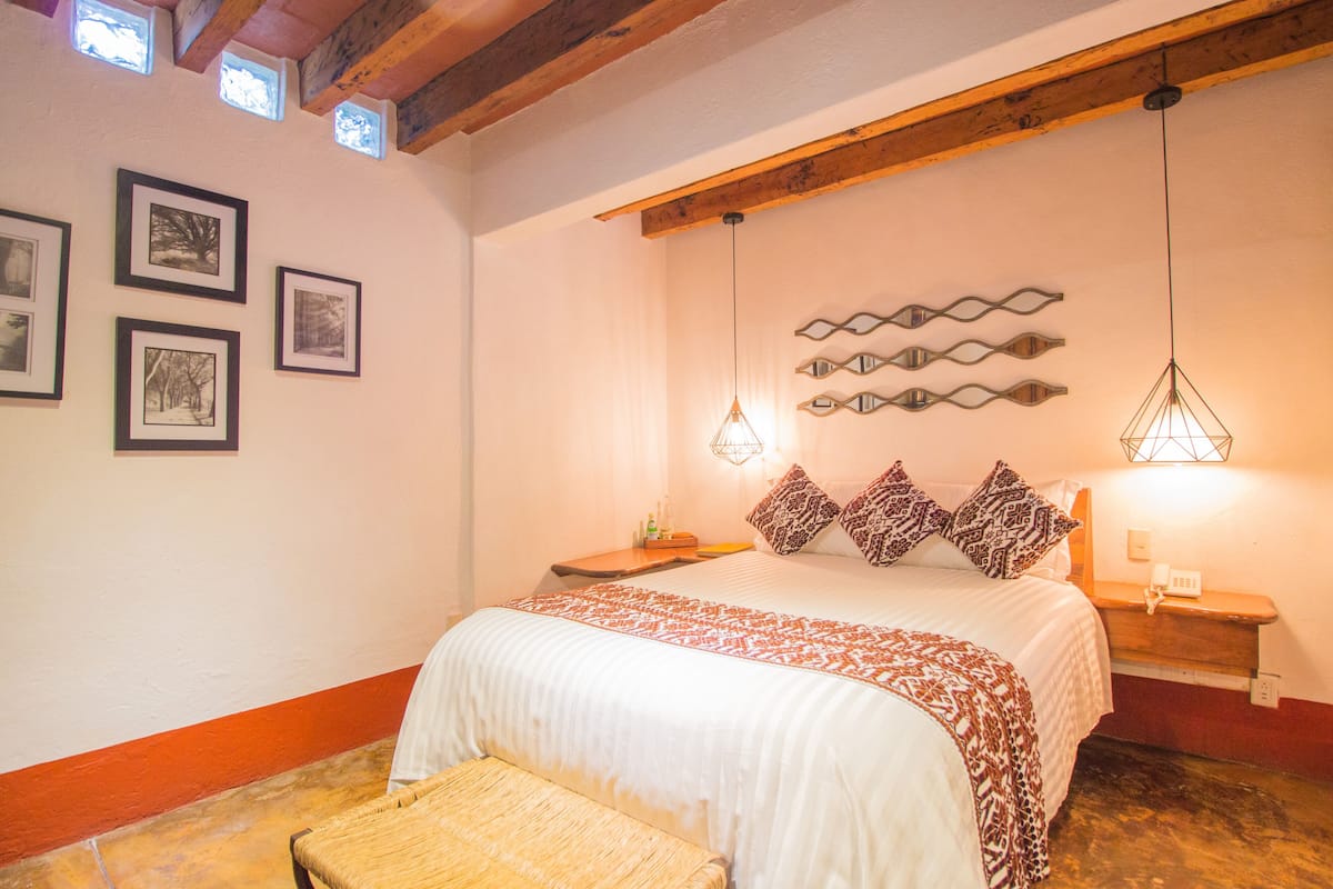 A bedroom with a bed, a bench, framed pictures on the wall, and a wooden ceiling.