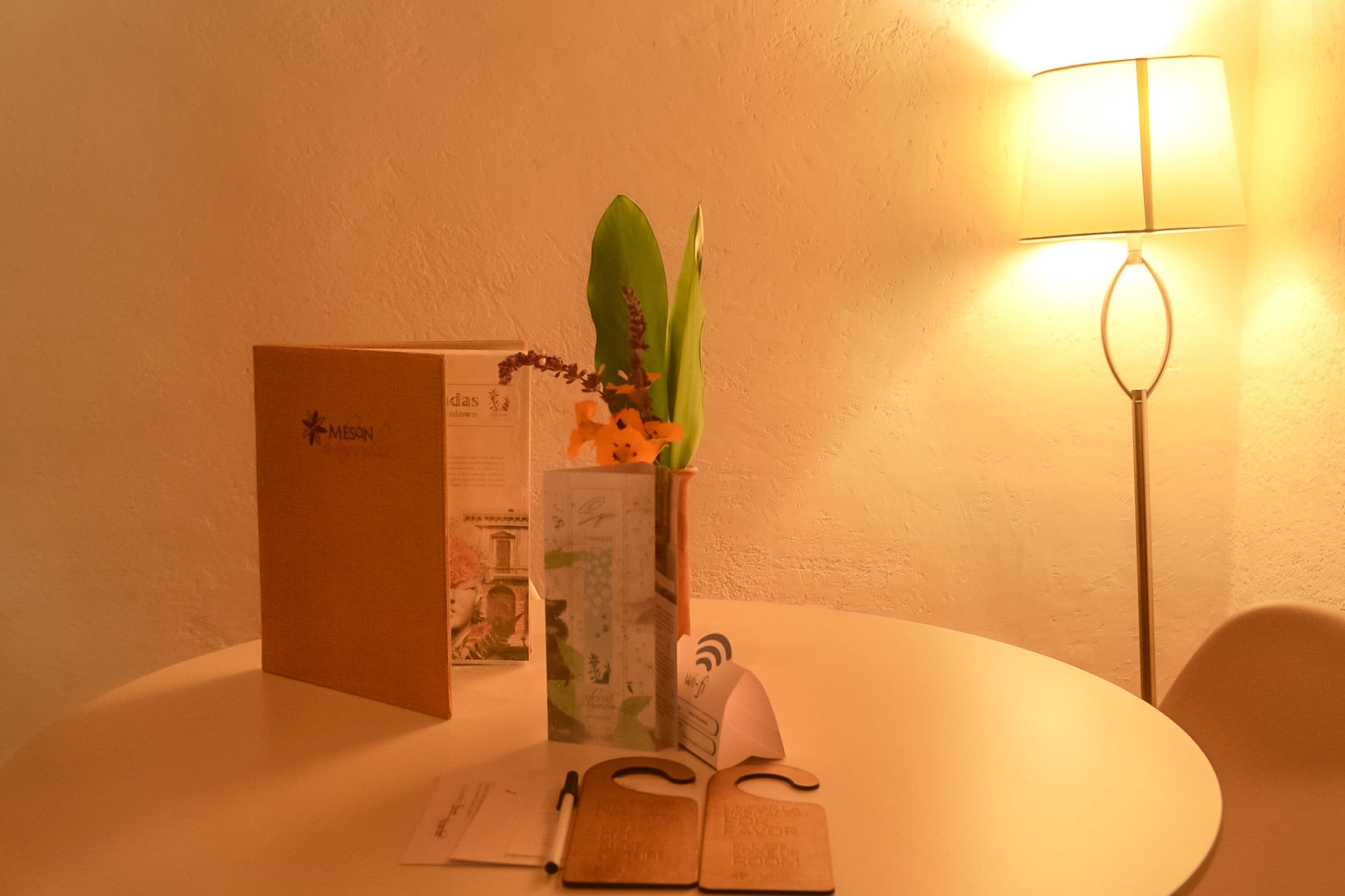 Une table avec une brochure, un stylo, un carnet et un vase de fleurs.