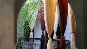Una ventana en arco con cortinas drapeadas, una planta en maceta y una barandilla de hierro forjado.