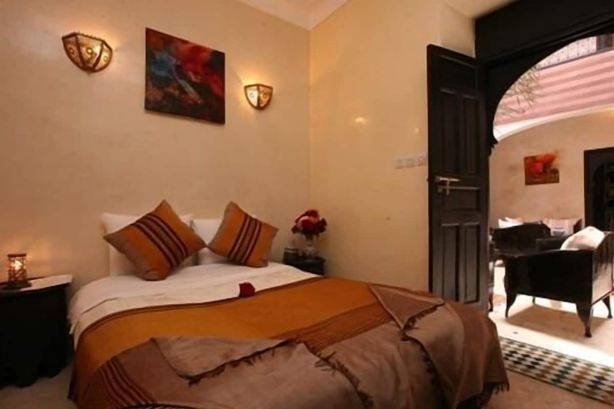 A bedroom with a large bed, two wall sconces, a painting, and a door leading to another room.