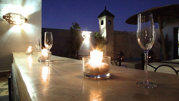 Una mesa con velas y copas de vino, una torre al fondo y un cielo vespertino despejado.