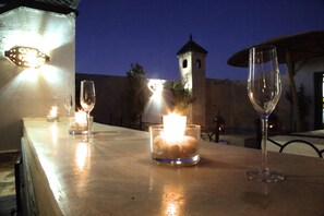 A table with candles and wine glasses, a tower in the background, and a clear evening sky. - Riad Dar Ftouma (Marrakech)