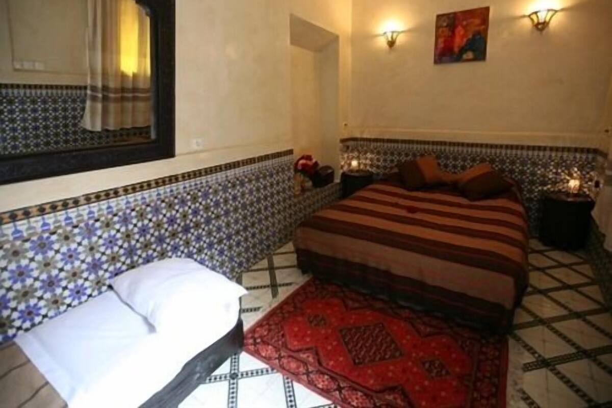 A bedroom with a bed, a nightstand, a mirror, and a wall with a decorative tile border.