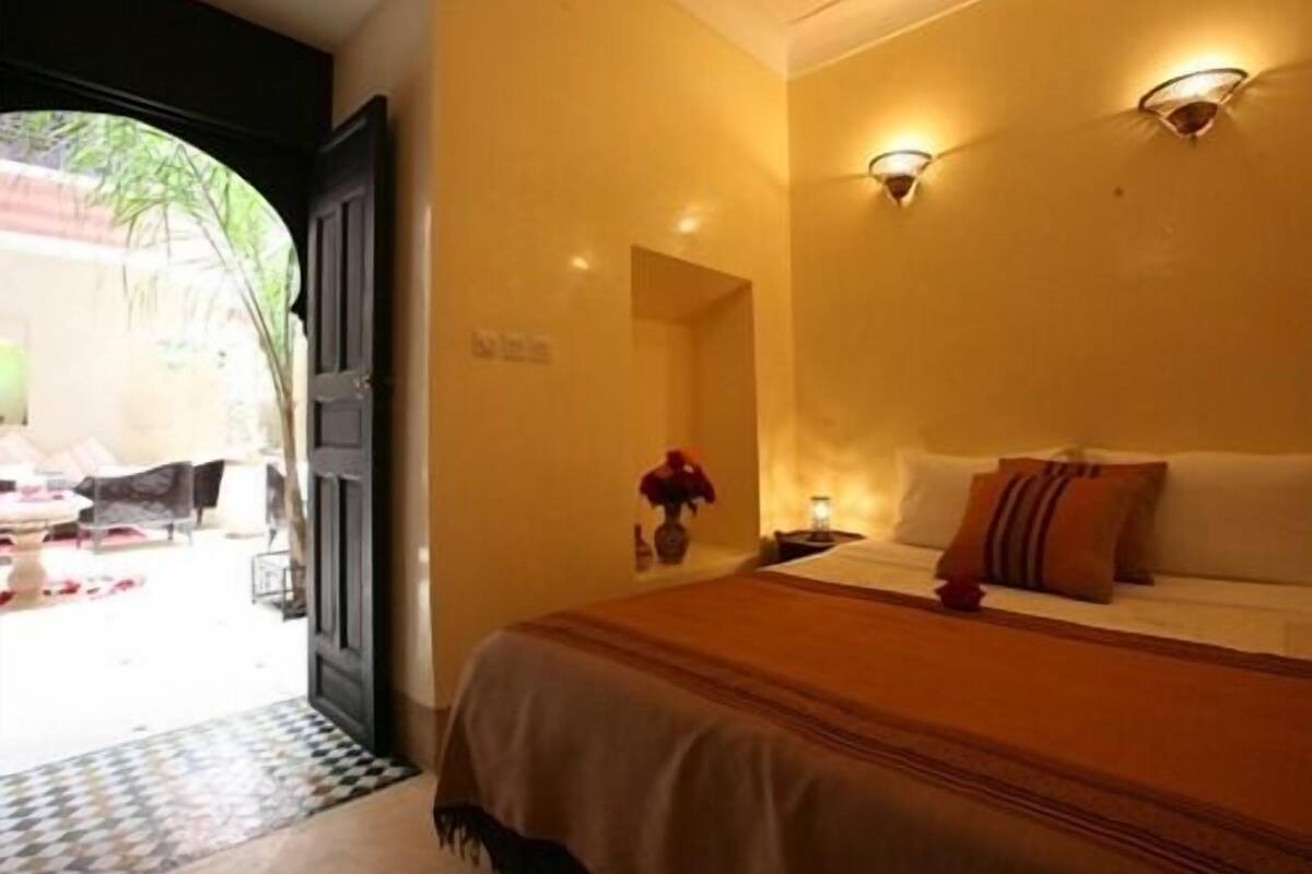 A hotel room with a bed, a nightstand, and a wall-mounted light fixture.