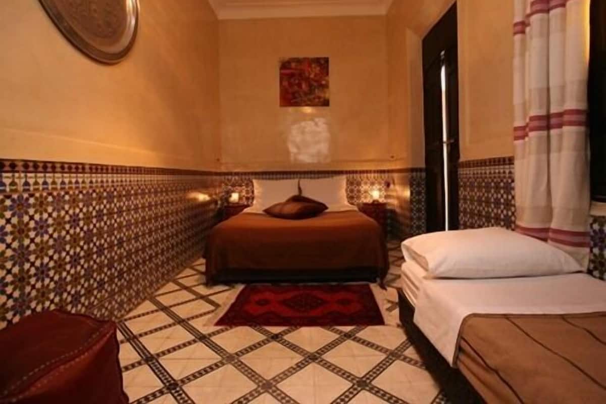A hotel room with a bed, a small table, a chair, and a decorative wall piece.