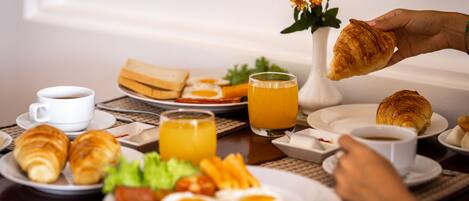 Un desayuno con cruasanes, huevos y zumo de naranja sobre una mesa.