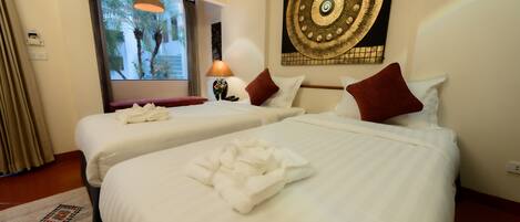 A hotel room with two beds, a large wall painting, a window with a view of palm trees, and a patterned rug.