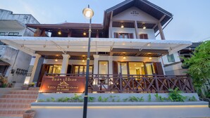 A two-story villa with a covered porch, a signboard, and a staircase leading to the entrance. - Villa Deux Rivieres (Luang Prabang)