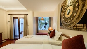 A hotel room with two beds, a large decorative wall piece, a window with a view of palm trees, and a door leading outside. - Villa Deux Rivieres (Luang Prabang)