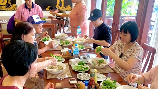 A group of people dining at a restaurant with a large table filled with various dishes, including bowls of soup and plates of food. - Villa Deux Rivieres (Luang Prabang)