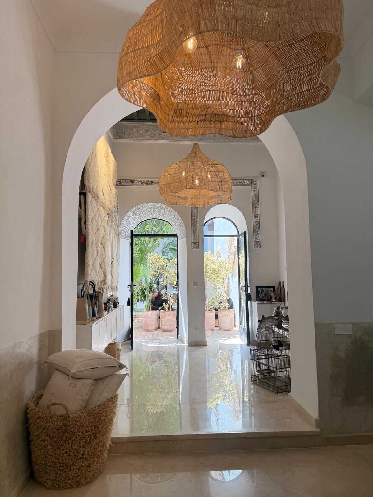 A spacious lobby with a high ceiling, large woven light fixtures, and a view of the outdoor area through arched doorways.