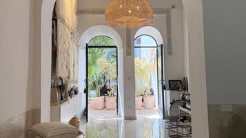 A spacious lobby with a high ceiling, large woven light fixtures, and a view of the outdoor area through arched doorways.
