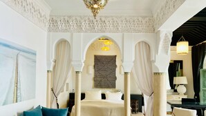 A luxurious bedroom with a four-poster bed, a sofa, a chair, and a glass coffee table. - Riad Rafaele & Spa (Marrakech)