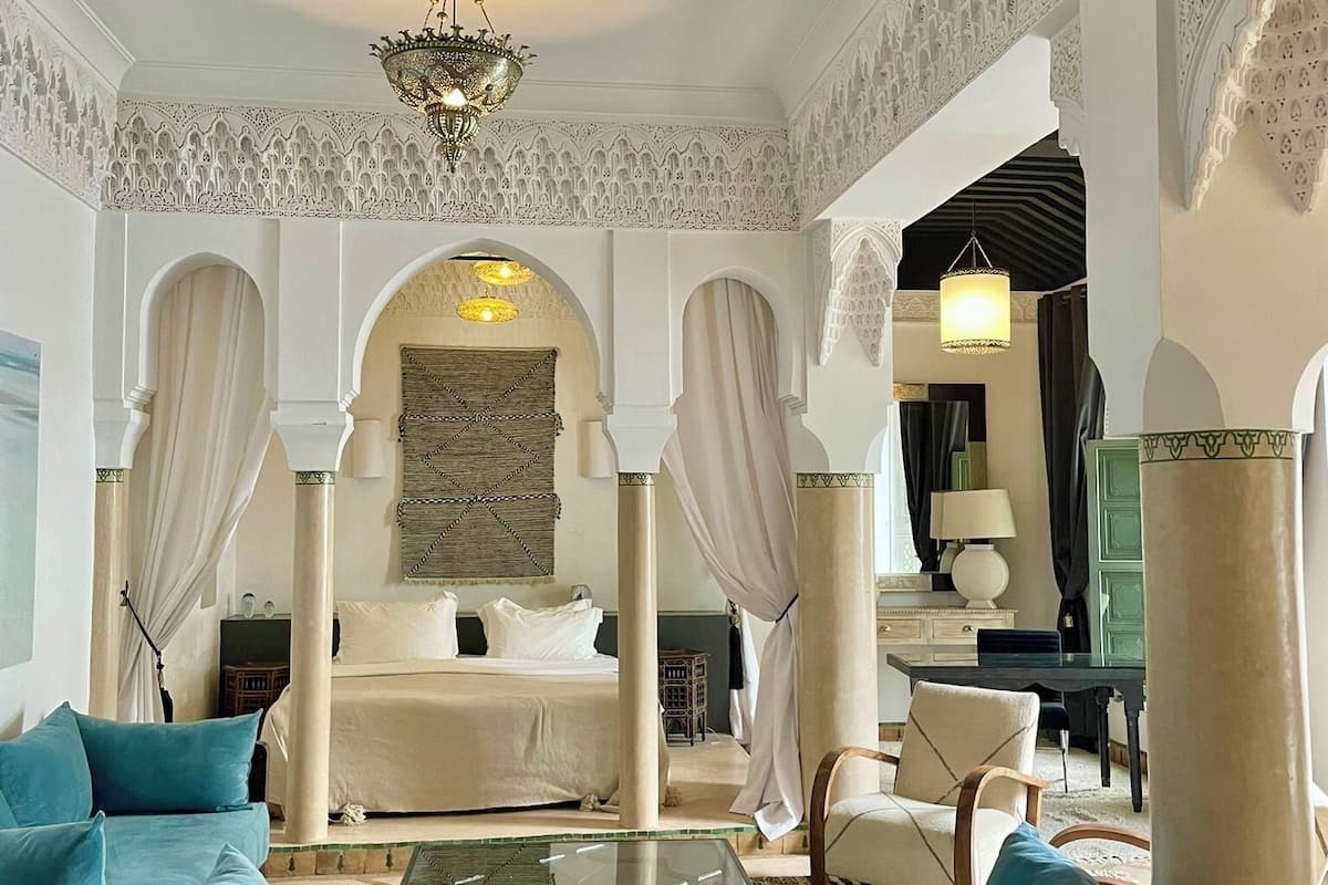 A luxurious bedroom with a large bed, a sitting area with a sofa, and a dining table.