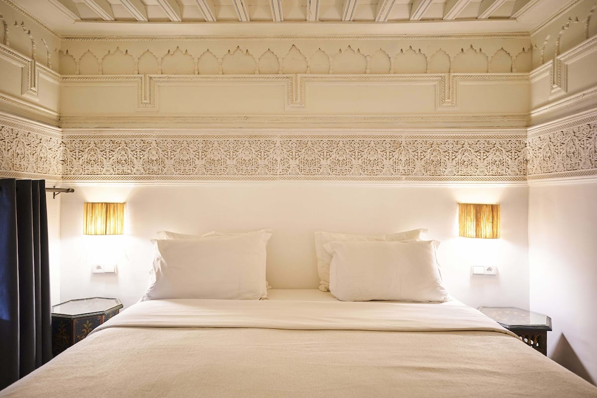 A hotel room with a large bed, two bedside tables, and ornate ceiling detailing.