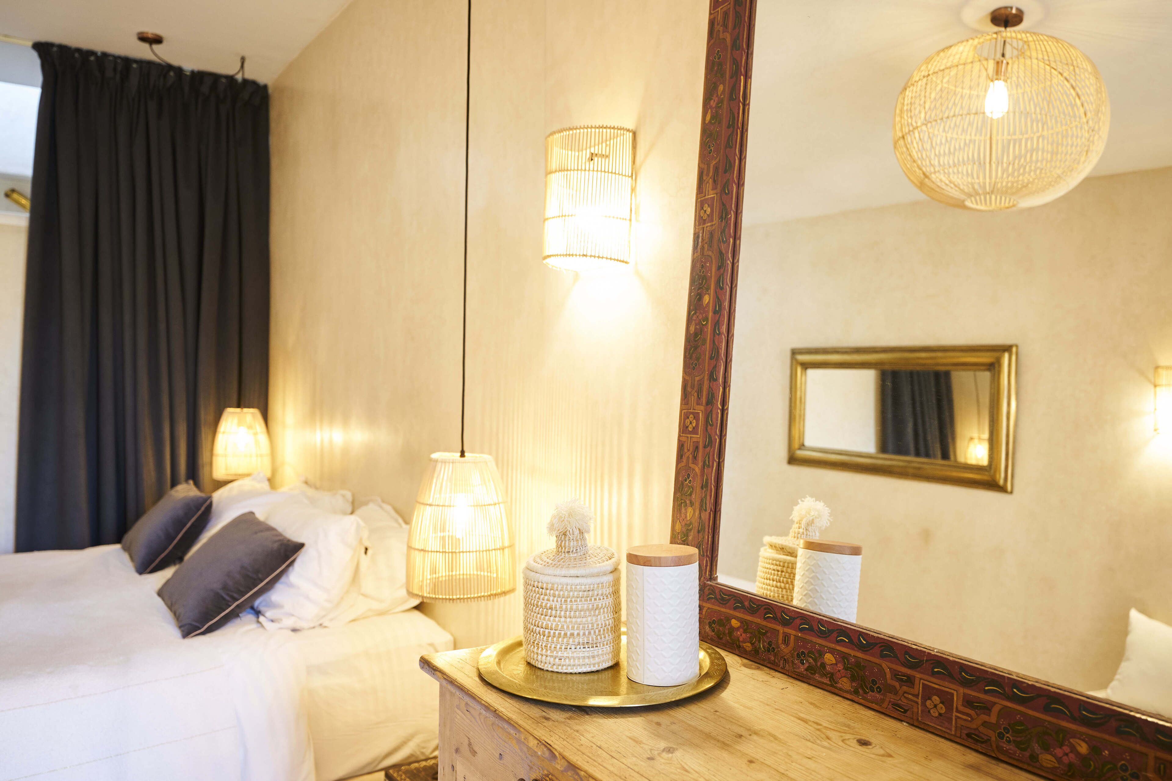 Habitación de hotel con cama, lámparas de noche, un espejo y una bandeja con objetos decorativos.