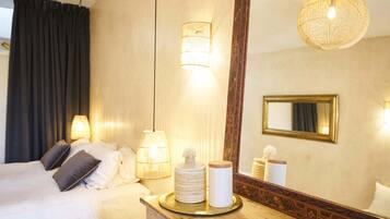 Habitación de hotel con cama, lámparas de noche, un espejo y una bandeja con objetos decorativos.