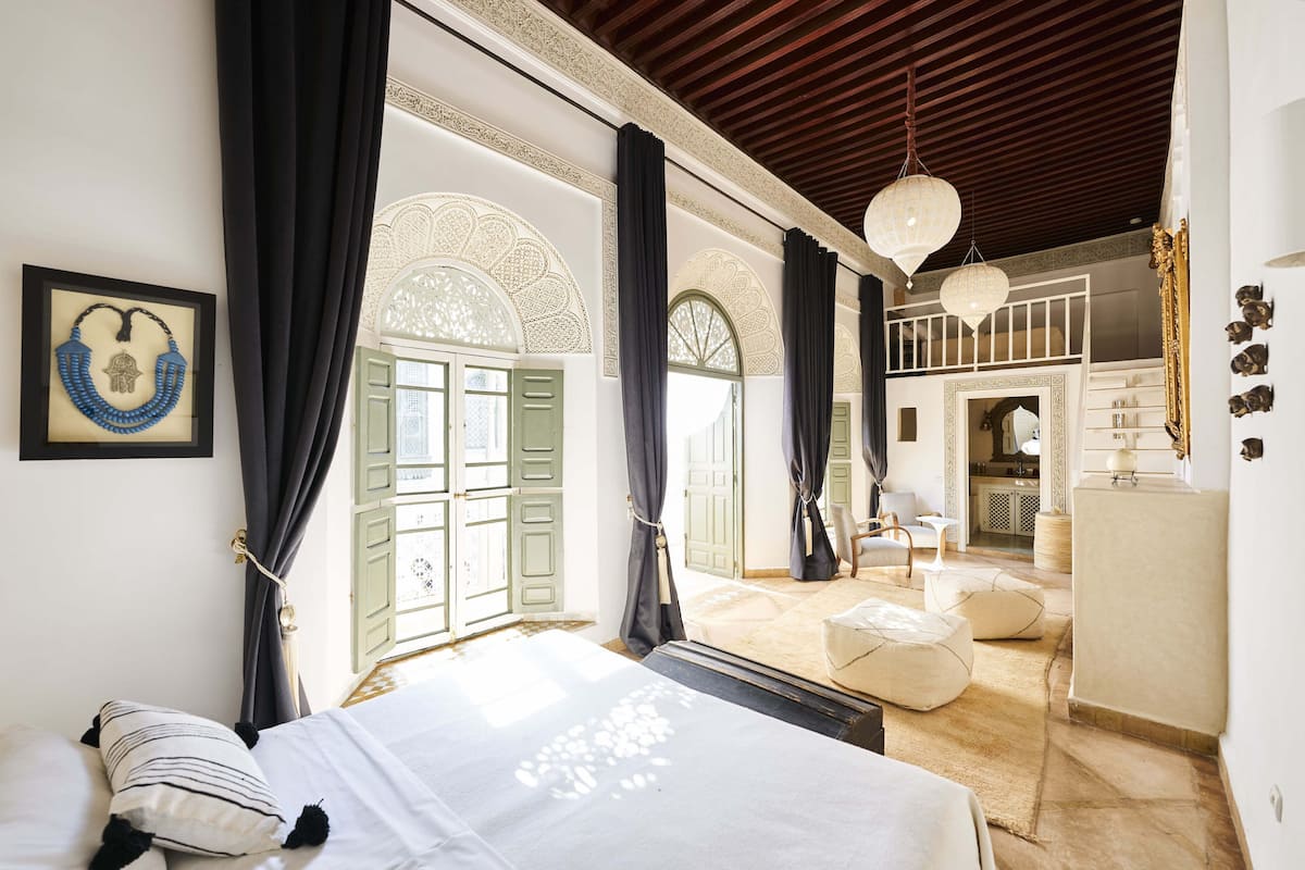 A bedroom with a bed, curtains, a mirror, and a view into the living area.