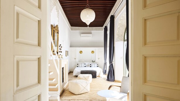 A well-lit bedroom with a bed, bedside tables, a hanging light fixture, and a view of the adjacent bathroom. - Riad Rafaele & Spa (Marrakech)