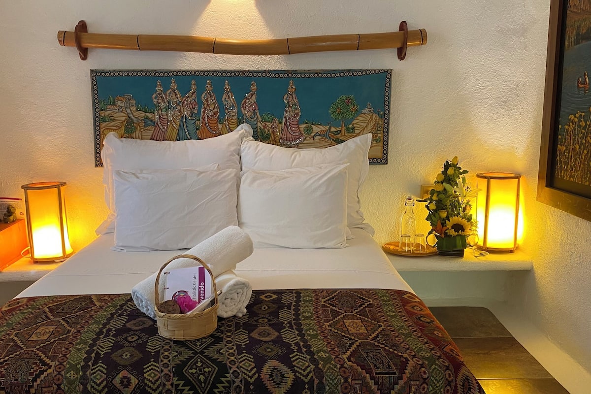 Una cama bien tendida con sábanas blancas, un cabecero decorativo y una alfombra estampada.
