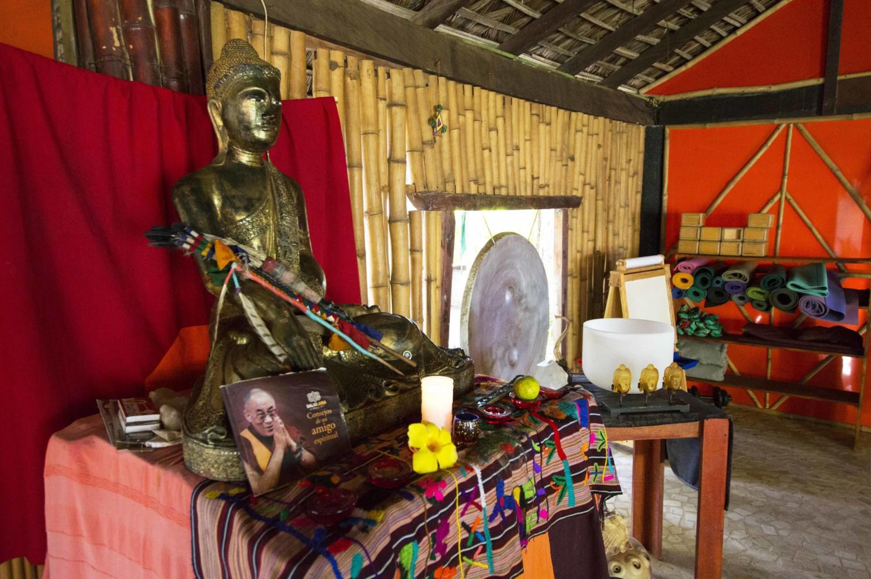 Una habitación con una estatua de Buda, un espejo, una vela blanca y una mesa con diversos objetos.
