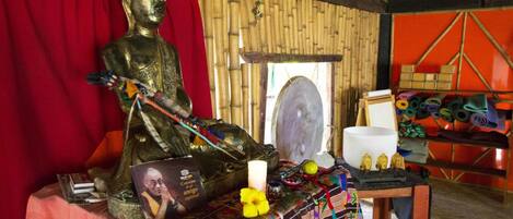 Una habitación con una estatua de Buda, un espejo, una vela blanca y una mesa con diversos objetos.