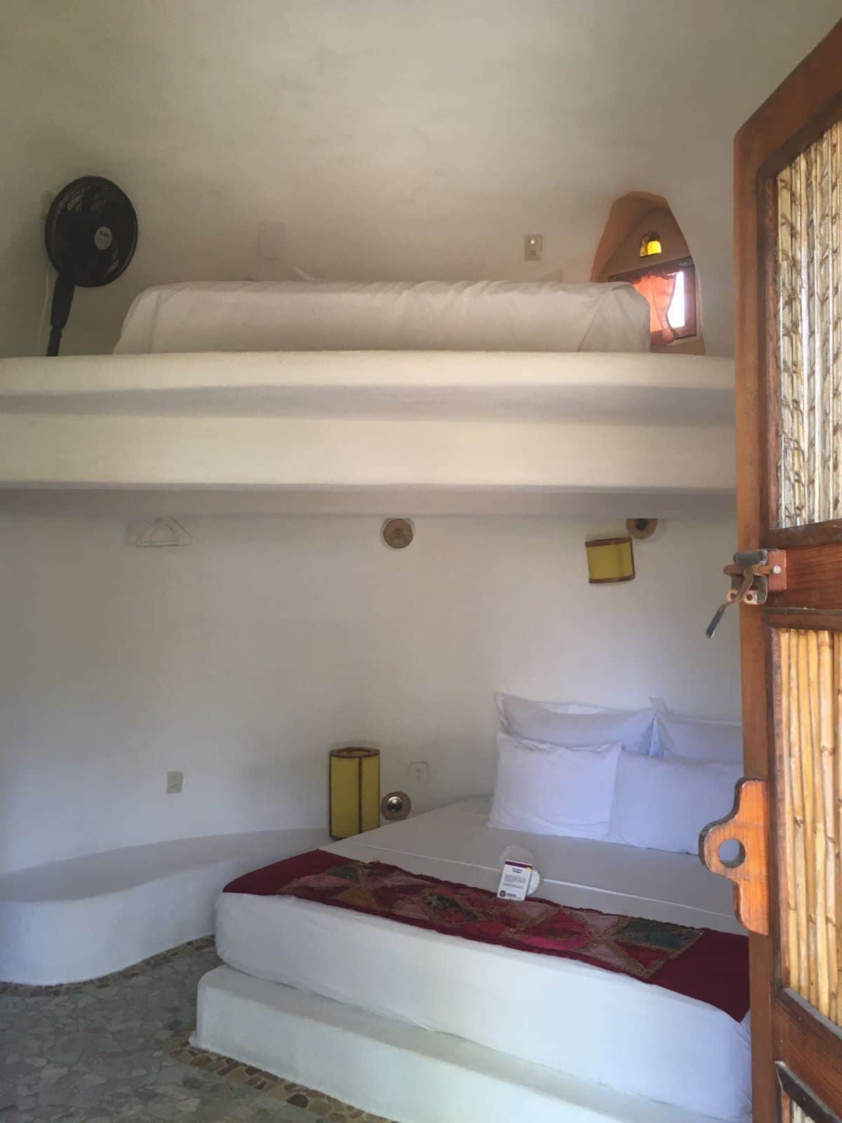 Habitación tipo dormitorio con literas, una mesita de noche pequeña, una lámpara y una ventana con vistas.