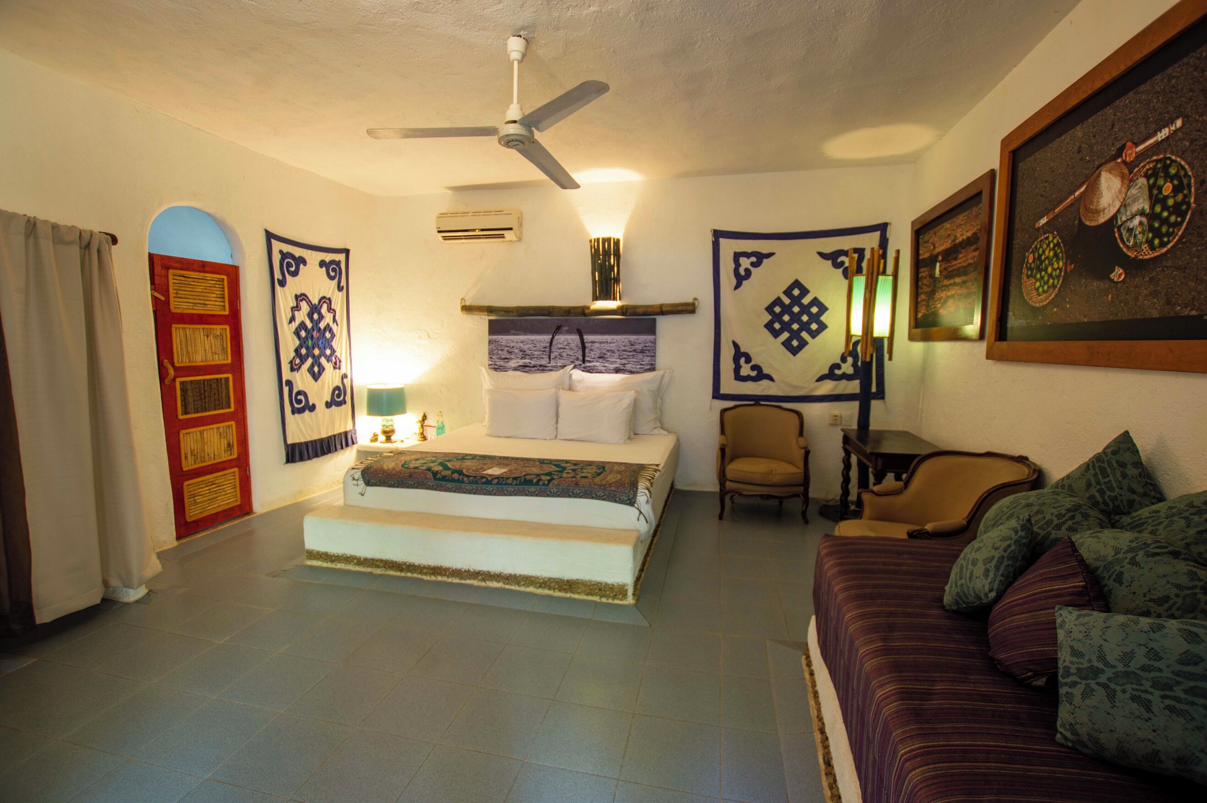 A bedroom with a bed, a chair, a sofa, a ceiling fan, and a wall with decorative panels.