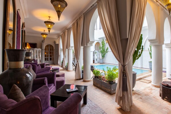 A luxurious lounge area with plush seating, a large vase, and a pool view. - Riad Shemsi (Marrakech)