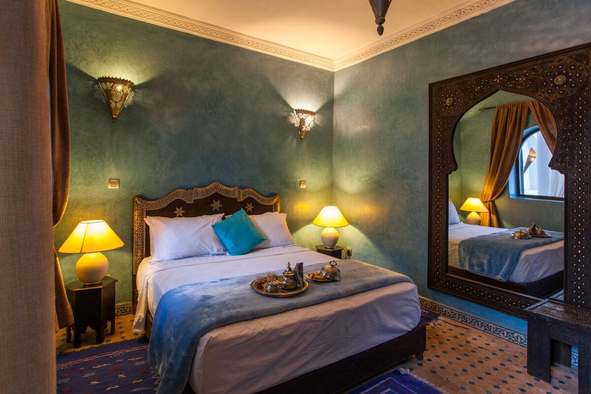 A bedroom with a large bed, two bedside lamps, a mirror, and a tray of tea and sugar on the bed.