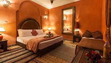 Habitación de hotel con una cama grande, una zona de estar, un espejo y apliques decorativos en la pared.