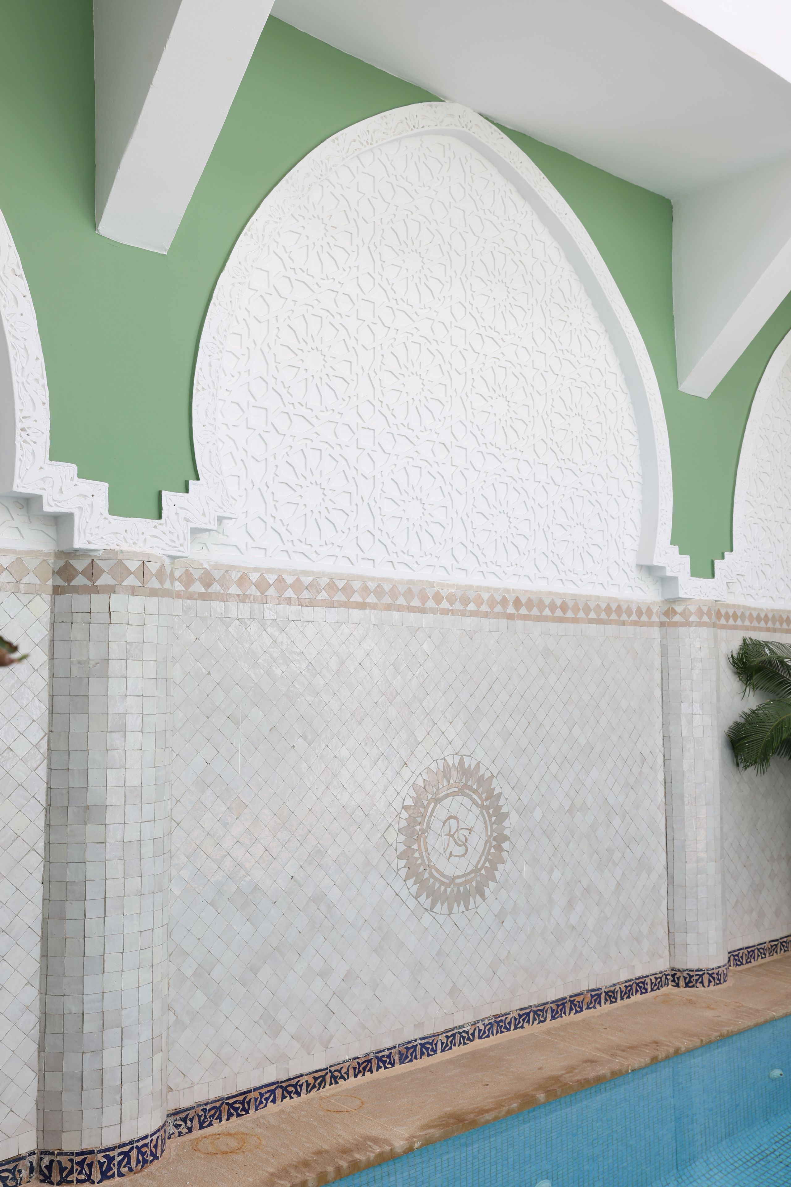 Zona de piscina con pared de azulejos que presenta un diseño geométrico y un emblema circular.