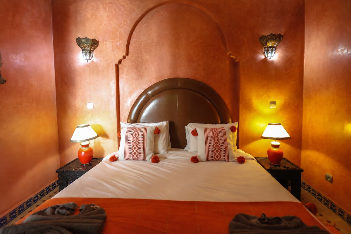 A hotel room with a large bed, two bedside lamps, decorative pillows, and a headboard with an arch design.