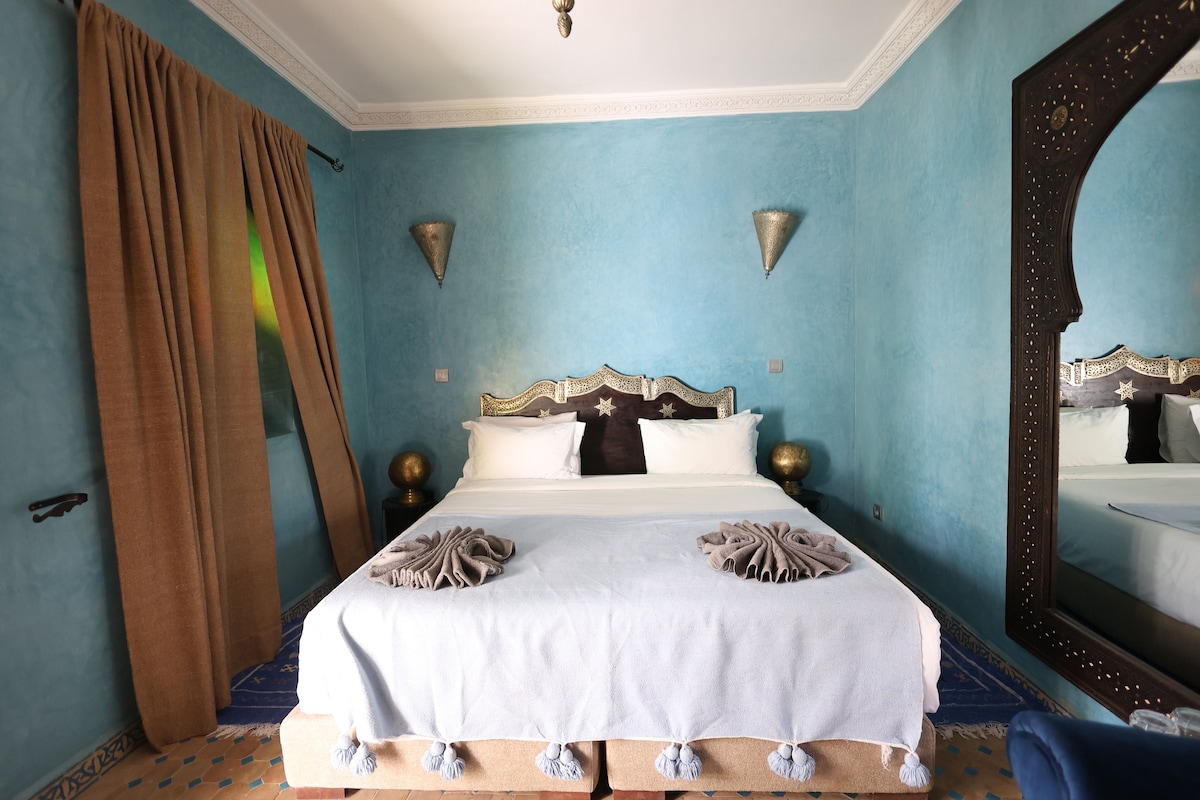 A bedroom with a bed, curtains, wall sconces, and a large mirror.