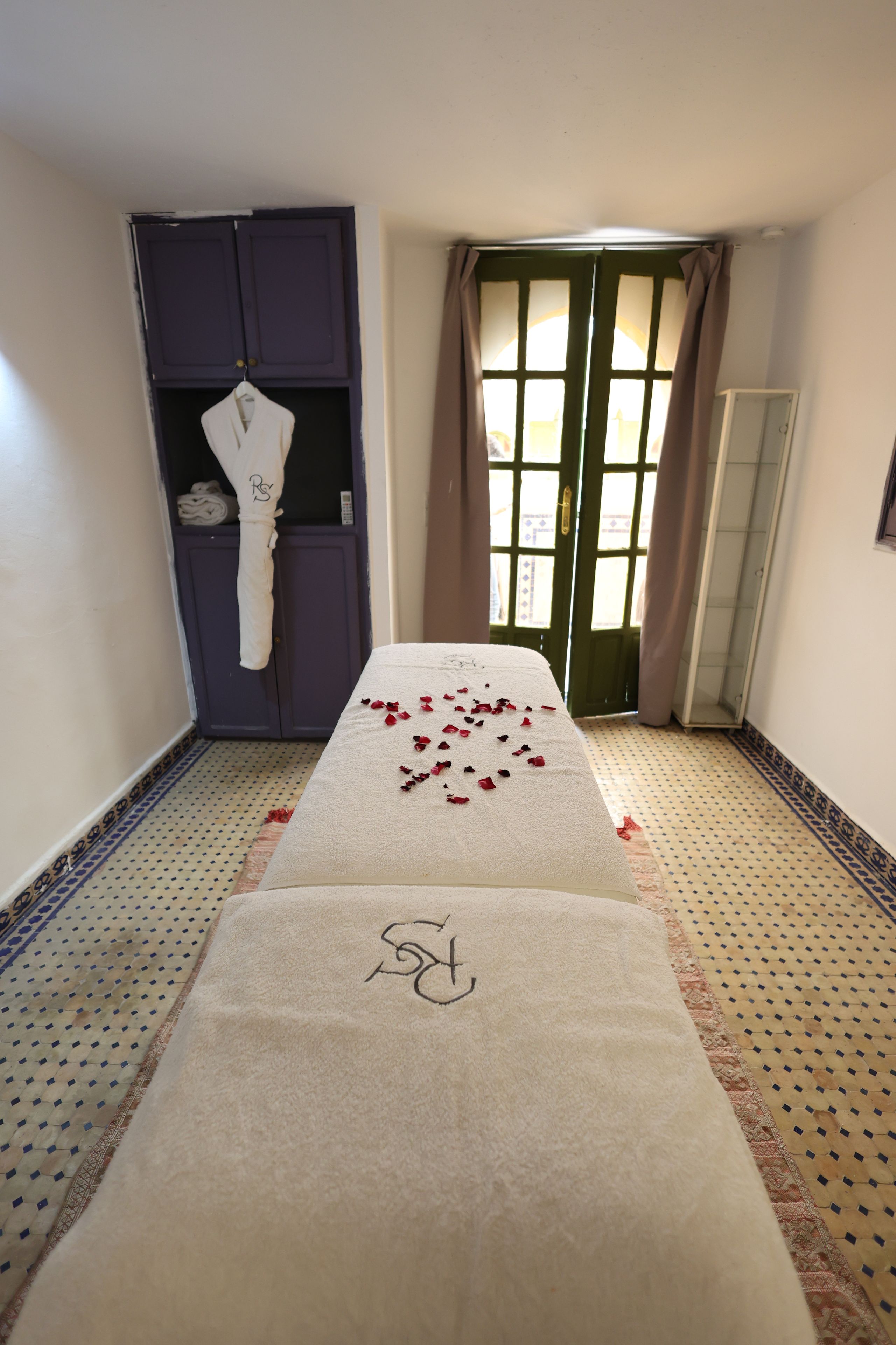 Habitación de hotel con un pasillo que conduce a una puerta, una bata colgada en un perchero y una toalla con un monograma en el suelo.